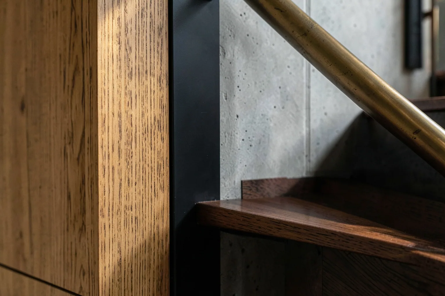 Detail of custom vertical-grain fir millwork meeting board-formed concrete and blackened steel with a patinated bronze handrail in a high-end Pacific Northwest home